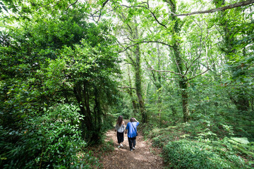 a lady and a young girl walk through the field, they are surrounded by lush green trees
