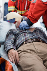 Selective focus of senior man lying in ambulance car near paramedics doing cardiopulmonary resuscitation