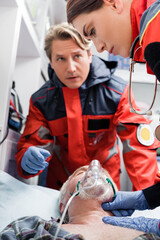 Selective focus of paramedic checking pulse of patient in oxygen mask near colleague in ambulance auto