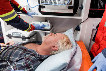 Selective focus of elderly patient lying near paramedics in latex gloves in ambulance car © LIGHTFIELD STUDIOS