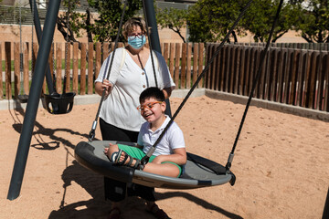 disabled child in swing set with mother wearing a pandemic coronavirus protective mask