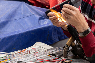 Hands of a glass blower blowing a piece of glass tubes using fire and high temperature. Glass manufacturing workflow.