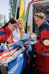 Fototapeta na wymiar Selective focus of paramedics holding stretcher with elderly patient near doctor and ambulance car