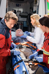 Fototapeta na wymiar Selective focus of paramedics and doctor standing near senior patient on stretcher and ambulance car
