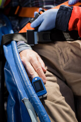 Cropped view of paramedic in latex gloves locking belt of stretcher near patient with heart rate monitor