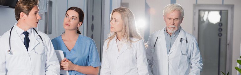 Panoramic shot of doctor talking to colleagues and nurse with digital tablet in hospital