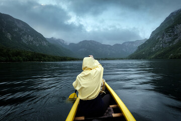 Rainy day boat ride. Rear view of woman in yellow raincoat paddling canoe. Active, adventure, outdoors, canoeing, kayaking