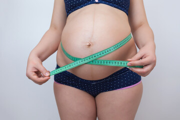 A pregnant woman measures her belly with a measuring tape