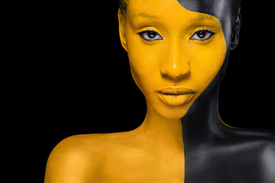 Face art. Woman with black and yellow body paint. Young african girl with colorful bodypaint. An amazing model with yellow makeup. Closeup face.
