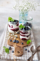 Vasetti di yogurt con confettura di mirtilli e mirtilli freschi e menta su un piano di legno