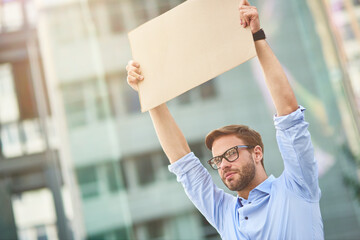 Protesting outdoors. Portrait of a young male activist wearing blue shirt and eyeglasses holding...
