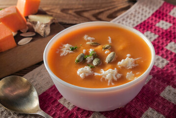  Pumpkin cream soup close up with cheese and seeds on a wooden table on a red checkered tablecloth....