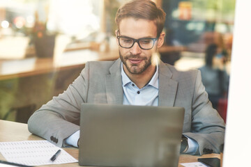 Front view of a young busy caucasian businessman or male freelancer using laptop while working remotely in cafe