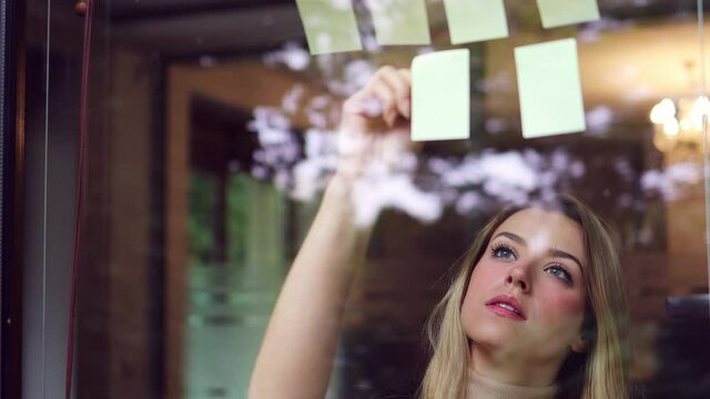 Young businesswoman brainstorming with notes on a glass wall in an office
