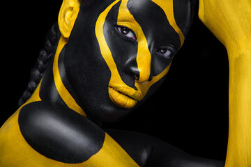 Gesichtskunst. Frau mit schwarzer und gelber Körperbemalung. Junges afrikanisches Mädchen mit bunter Körperfarbe. Ein erstaunliches Modell mit gelbem Make-up. Nahaufnahme Gesicht. © Mike Orlov