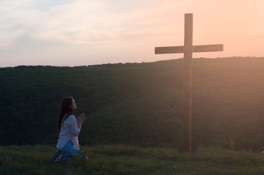 Young Woman Kneeling. Praying. Hands In Prayer. Near The Wooden Cross.