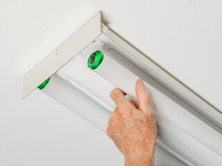 Electrician changing fluorescent light bulb in ceiling light fixture. Man replacing burned out fluorescent light tube.