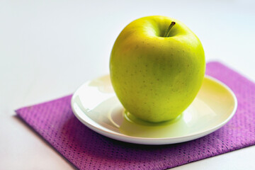 A ripe yellow apple lies on a saucer on a white background.