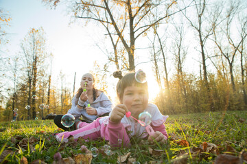 Two sisters lying on the ground in autumn park and blowing soap bubbles