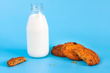 Bottle with milk and oatmeal cookies on a blue background.