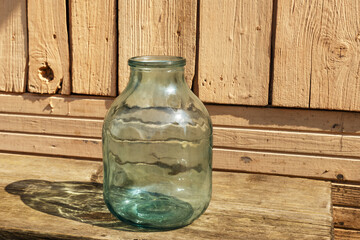 Empty glass jar. There is a three-liter jar on a wooden bench near the wall of the house.