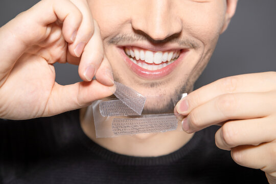 smiling man unwrapping and pulling whitening stripes from foil ready to apply to his teeth