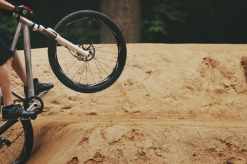 sporty bicycle rider taking off powerfully with mountain bike at dirt jumpline in the woods -...