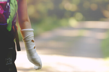 Child or teenage kid with forearm in plaster cast goes hiking happily on forest path in bright sun...