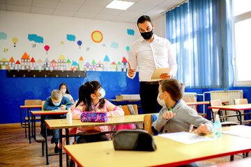 Elementary schoolchildren writing at the desk in the classroom. Education during epidemic.