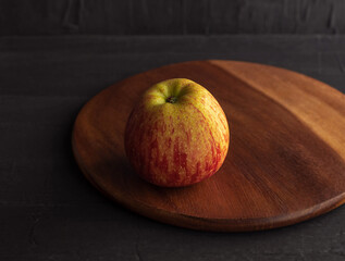 One small apple rests on a round wooden cutting board