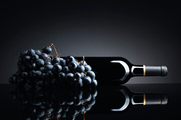 Bottle of red wine and a bunch of grapes on a black reflective background.