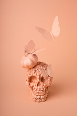 Minimal layout made with skull, butterflies and pumpkin on orange background. Creative Halloween concept. Magic surreal image, witch ritual atmosphere.