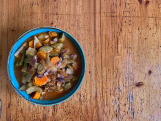 Vegetable minestrone soup in a blue bowl on a rustic wooden table
