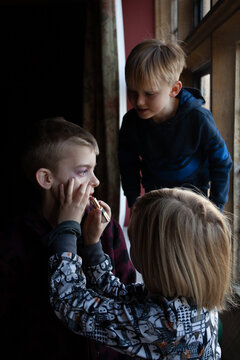 A little girl applies lipstick on her brother while their cousin looks on.