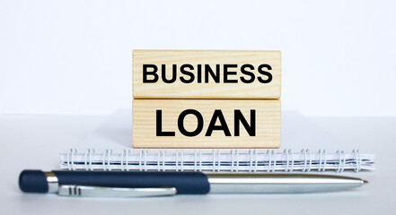 Obraz premium The text Business Loan on a bar of jenga wood, lying on a Notepad with a metal blue pen