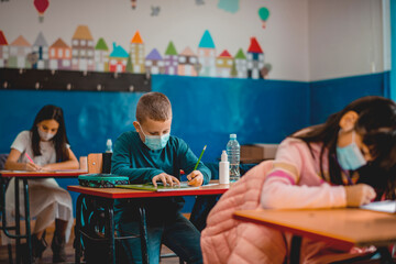 Elementary schoolchildren wearing a protective face masks  in the classroom. Education during epidemic.