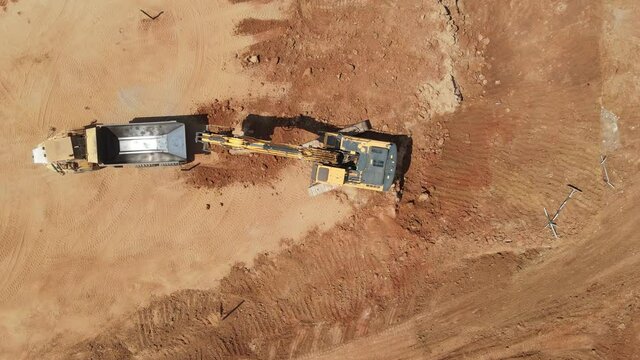 Aerial view of heavy machinery, excavator scoop loads a  articulated truck, heavy equipment top down footage
