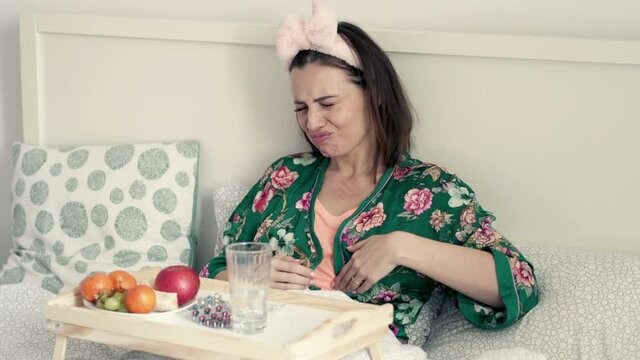 Young woman gets stomach ache during breakfast in bed, 4K
