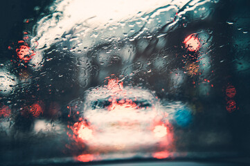 Blurred city street during dark rainy day, shoot through car window with drops of rain