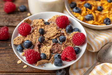 Granola with blueberries and raspberries in white bowl on dark white desk.