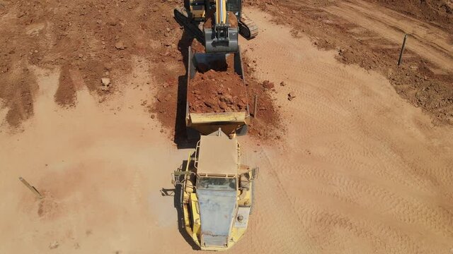 Aerial view of heavy machinery, excavator scoop loads a  articulated truck, heavy equipment top down footage
