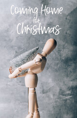 Coming home for Christmas text. Wooden mannequin is carrying tiny christmas tree on its back, concept of preparation for Xmas holidays, going home for festive time concept
