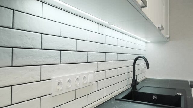 Kitchen sink and faucet. Simple well designed modern white wooden kitchen interior. Ceramic tiles on the wall and wooden countertop. Dolly camera move 4k