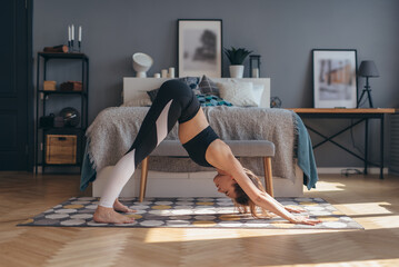 Fit woman doing stretching workout in morning at home. Downward facing dog yoga pose - obrazy, fototapety, plakaty