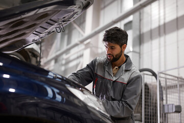 bearded auto mechanic engine performance in the hood of car, going to repair it, conducts...