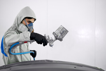 young confident caucasian auto mechanic man spraying varnish at car, in protective mask and eyewear at work. automobile, car industry. wash and coating business with ceramic coating polishing