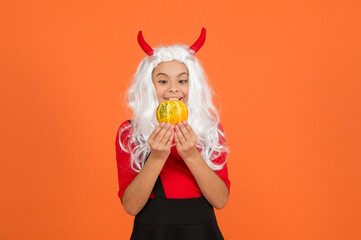 Happy girl on Halloween wear funny carnival costume and devil horns indoor holding pumpkin, halloween magic