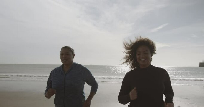 Two plus size females exercising outdoors on beach at sunrise, Obese black women sports training body positive