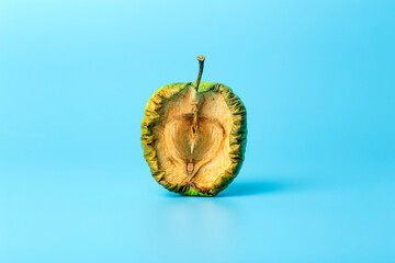 Old dried apple on a blue minimal background. Spoiled and shriveled fruits and vegetables. Old age...