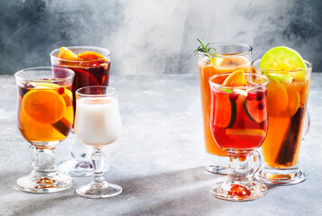 Selection of autumn or winter alcoholic hot drinks and cocktails - mulled wine, glogg, grog, eggnog, warm ginger ale, hot buttered rum, punch, mulled apple cider on gray background, copy space